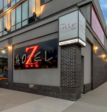 A modern street-side bar/restaurant with red seating along the wall, large illuminated sign, brick accents, and a sign reading &ldquo;the CELLAR&rdquo; on the corner. Top it at 140 characters, ending with a period.