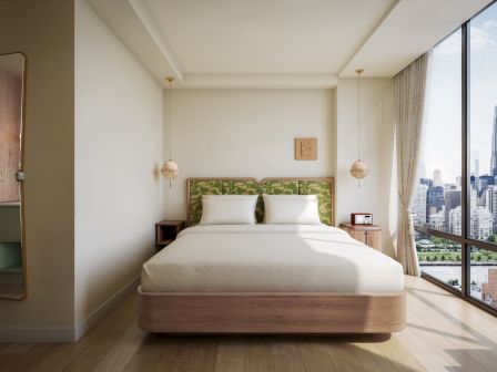 A bright modern bedroom with a double bed, patterned headboard, pendant lamps, and a city skyline view through large windows.