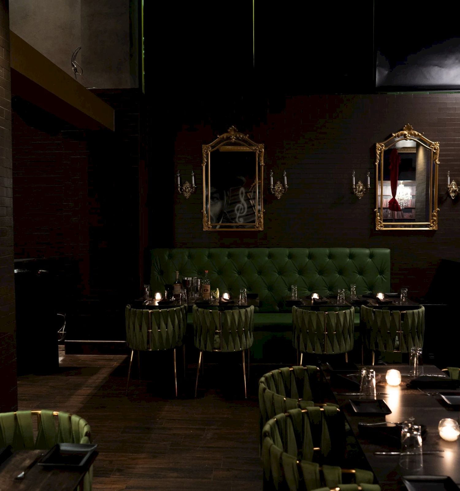 A dim lounge restaurant with green tufted booths, candlelit tables, and ornate gold mirrors reflecting the room.