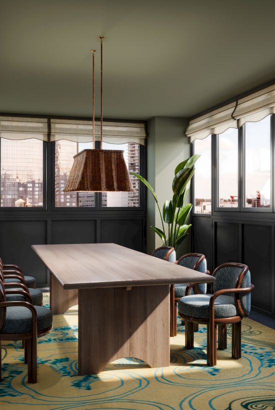 Bright dining room with a wooden table and chairs, pendant light, patterned rug, and large windows overlooking a city.
