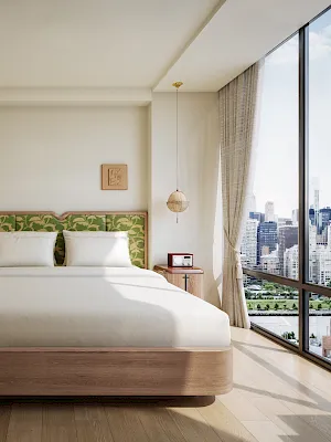 Bright hotel bedroom with a large bed, patterned headboard, pendant lights, and big window showing the city skyline.