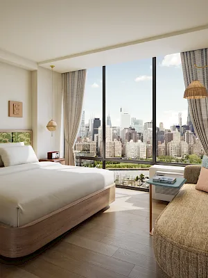 A modern bedroom with a large bed, cushioned chairs/sofa, hanging woven lamps, and tall windows showing a city skyline.